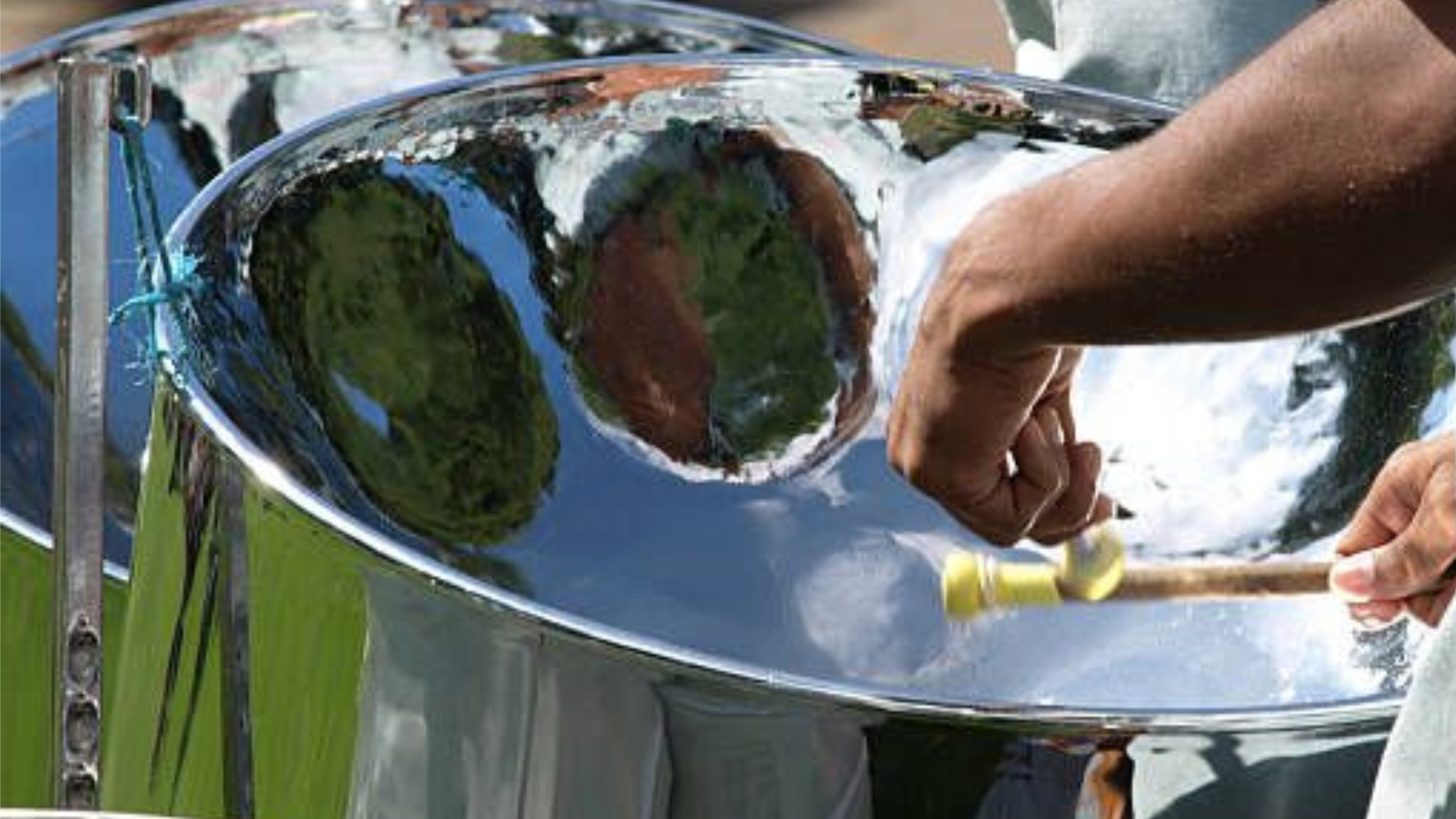 Person playing a steel drum with a close-up of hands and steelpan